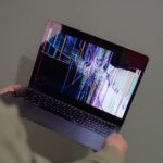 A broken laptop screen displayed with colorful glitch being held by a person. — Photo by Beyzanur K.