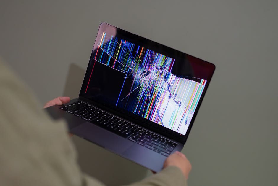 A broken laptop screen displayed with colorful glitch being held by a person. — Photo by Beyzanur K.