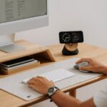 A clean and modern desk setup featuring a computer, clock, and accessories in a home office. — Photo by Mateusz Haberny